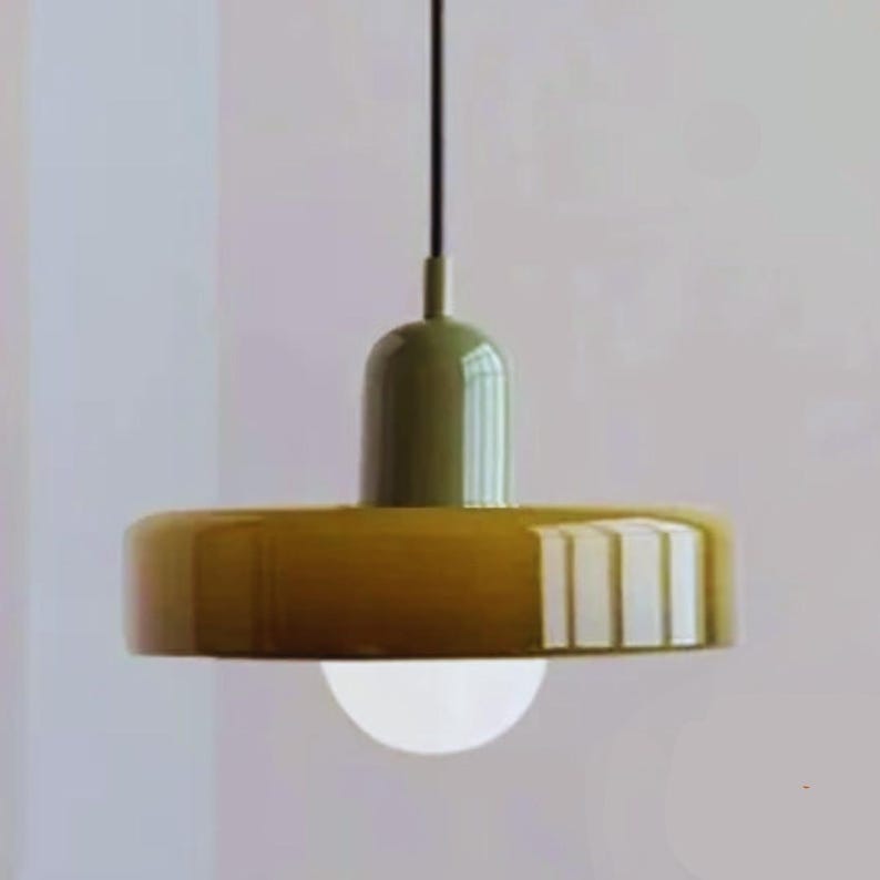 May include: A modern pendant light fixture with a round, olive green top and a wide, mustard yellow shade. A white, spherical light bulb hangs below. The fixture is suspended from a black cord.