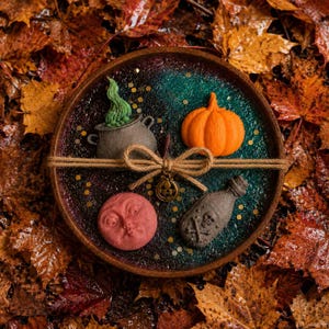 May include: A round tray with a dark green and black glittery surface featuring a grey cauldron with green smoke, an orange pumpkin, a red moon face, and a grey potion bottle with a skull and crossbones, tied with twine and a pumpkin charm.