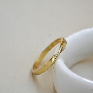 Könnte beinhalten: Ein goldfarbener Ring mit einem gedrehten Design. Der Ring liegt auf einer weißen Oberfläche. Das Design des Rings weist eine durchgehende, fließende Drehung auf, die einen einzigartigen und eleganten Look erzeugt. Dieses Schmuckstück eignet sich für den Alltag oder besondere Anlässe.