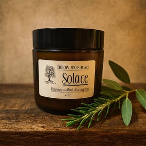 Könnte beinhalten: Ein braunes Glas mit schwarzem Deckel, beschriftet mit "Talg-Feuchtigkeitscreme Solace Rosemary-Mint-Eucalyptus 113 g." Ein Zweig Rosmarin und Eukalyptusblätter liegen neben dem Glas auf einer Holzoberfläche.