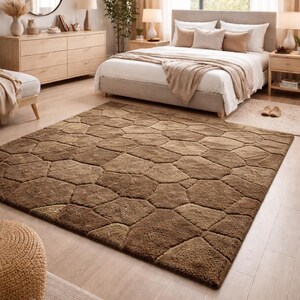 May include: A large, brown area rug with a geometric pattern dominates a bedroom scene. The rug's design resembles irregularly shaped stones. The room features a bed, dresser, and side tables, all in neutral tones, creating a warm and inviting atmosphere.