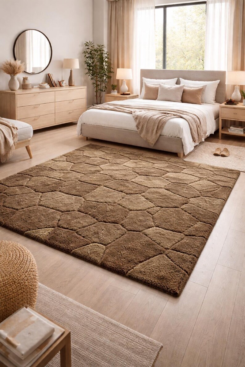 May include: A large, brown area rug with a geometric pattern dominates a bedroom scene. The rug's design resembles irregularly shaped stones. The room features a bed, dresser, and side tables, all in neutral tones, creating a warm and inviting atmosphere.