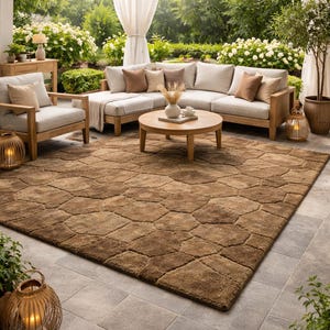 May include: An outdoor living space featuring a large brown geometric patterned rug, a light-colored sectional sofa with throw pillows, and wooden armchairs. A round wooden coffee table and a woven pendant light complete the scene, with lush greenery in the background.
