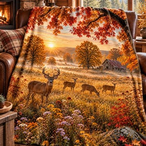 Könnte beinhalten: Eine weiche Wohndecke mit einem herbstlichen Landschaftsdruck, der einen Hirsch und drei Rehe auf einer goldenen Wiese zeigt. Die Szene umfasst eine rustikale Scheune, Bäume mit orangefarbenem Laub und einen Sonnenaufgang. Im Vordergrund blühen Wildblumen.