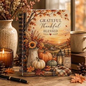 May include: A spiral-bound notebook featuring an autumn-themed illustration of pumpkins, a sunflower bouquet in a pitcher, and a lantern. The cover displays the text "GRATEFUL Thankful BLESSED" and "give thanks" with a sunset landscape background.
