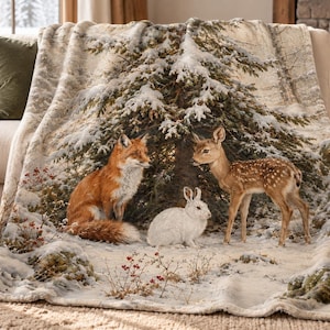Könnte beinhalten: Eine Plüschdecke mit einer winterlichen Waldszene, die einen Rotfuchs, einen weißen Hasen und ein geflecktes Rehkitz zeigt, die im Schnee unter einem großen, schneebedeckten Nadelbaum stehen. Das Design enthält kleine rote Beeren.
