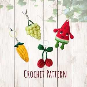 Op de afbeelding: Vier gehaakte fruit sleutelhangers: een gele maïskolf, een tros druiven, een paar kersen en een watermeloen schijf met armen en benen. De tekst "CROCHET PATTERN" is zichtbaar.