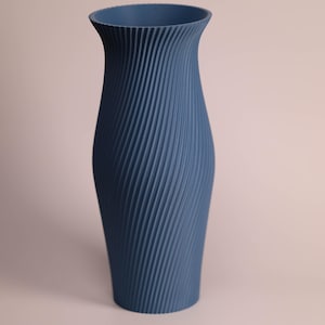 May include: A matte blue vase featuring a distinct vertical ribbed texture that spirals around the body. The vessel has a wide, flared opening at the top that tapers down into a slender neck, then widens toward the base in a smooth, curved silhouette.