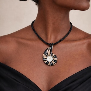 Può includere: Collana in corda nera con un pendente a forma di conchiglia Nautilus. Il pendente a conchiglia presenta strisce nere, crema e bianche e un motivo a spirale centrale. Un accessorio di moda.