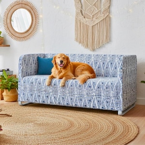 Puede incluir: Un sofá con estampado azul y blanco con un perro golden retriever acostado sobre él. Un cojín azul descansa sobre el sofá. Una alfombra redonda de yute está en el suelo. Un espejo decorativo y un tapiz de macramé están en el fondo.