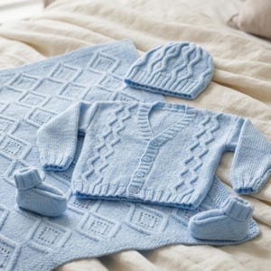 Può includere: Un set in maglia azzurra per neonati, composto da una coperta, un cappello, un cardigan e delle scarpine. La coperta presenta un motivo a rombi, mentre il cappello e il cardigan hanno un design a trecce. Le scarpine sono piccole e accoglienti.