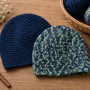 May include: Two handmade crochet beanies. One is a solid navy blue, the other is a mix of green, blue, and purple. A wooden crochet hook and a basket of yarn are also visible. The beanies are on a wooden surface.