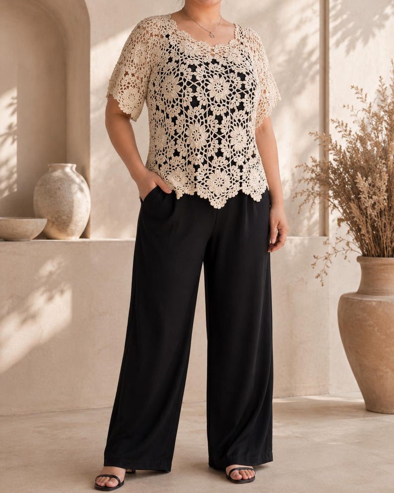 Puede incluir: Una blusa de crochet beige de manga corta con patr&oacute;n floral sobre una camiseta sin mangas negra, combinada con pantalones negros de pierna ancha con bolsillos laterales. La blusa de crochet tiene un cuello y dobladillo festoneados.