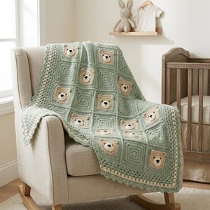 May include: A handmade, light green crochet baby blanket with a repeating pattern of teddy bear faces. The blanket is draped over a beige rocking chair. The teddy bear faces are beige with black eyes and noses. The blanket has a scalloped edge.
