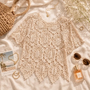 Puede incluir: Un top de ganchillo beige con un patr&oacute;n floral detallado, mangas cortas y un dobladillo festoneado. La prenda se muestra junto a un bolso de paja trenzada, un collar de cadena dorada, un anillo peque&ntilde;o de oro, gafas de sol marrones y un frasco.