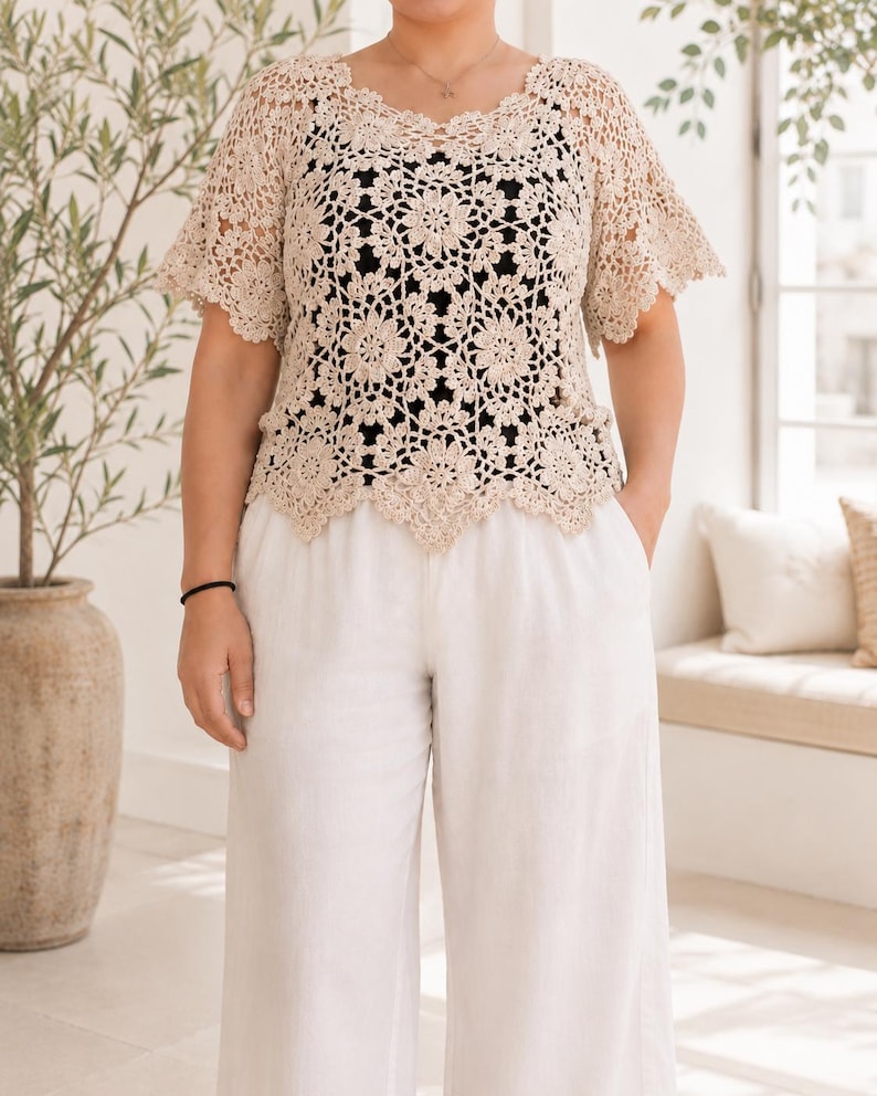 Puede incluir: Un top de ganchillo beige con un patr&oacute;n floral repetitivo, mangas cortas acampanadas y un dobladillo festoneado. La prenda se lleva sobre una capa base negra lisa y se combina con pantalones blancos holgados que tienen bolsillos laterales.