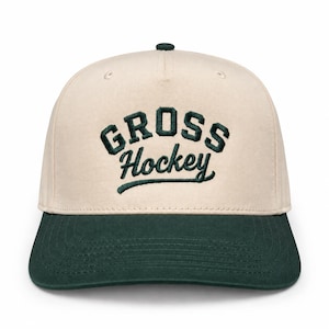 Peut inclure: Une casquette de baseball beige avec une visière vert foncé et un texte brodé vert foncé sur le devant qui indique GROSS Hockey. La casquette présente une calotte structurée avec un bouton vert foncé assorti sur le dessus et des œillets.