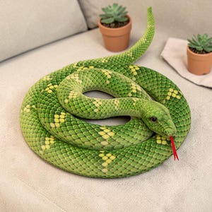 May include: A coiled plush snake toy in shades of green and yellow, with a red tongue. The snake is detailed with scale patterns and a realistic head. The toy is resting on a light-colored surface.