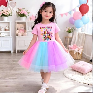 Może przedstawiać: Mała dziewczynka w różowej sukience z tęczową tiulową spódnicą. Sukienka ma nadruk z napisem "Hunters" i gwiazdą. Dziewczynka ma na sobie różową kokardę i białe buty.