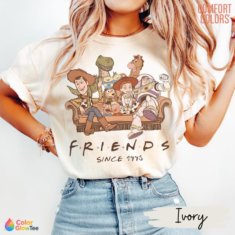 May include: An ivory t-shirt featuring a graphic of Toy Story characters sitting on a couch with the text "FRIENDS SINCE 1995" printed below. The design includes Woody, Buzz Lightyear, Jessie, Rex, Bullseye, Slinky Dog, and Mr. Potato Head.