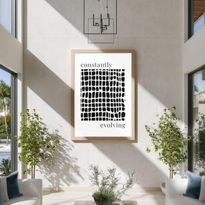Puede incluir: Una impresión artística enmarcada con las palabras "constantly evolving" en una fuente moderna. La obra de arte presenta un diseño abstracto en blanco y negro de formas irregulares. El marco es de color madera clara y la impresión cuelga de una pared blanca.
