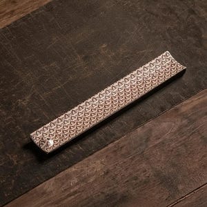 Peut inclure: Un long porte-encens rectangulaire en céramique avec un motif géométrique marron et blanc. Le support est légèrement incurvé et repose sur une surface en bois foncé. Le porte-encens est conçu pour recueillir les cendres.