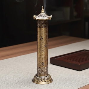 Peut inclure: Un brûleur d'encens en bronze avec un sommet en forme de pagode et une base décorative. Le corps cylindrique présente des motifs gravés et des caractères chinois. De la fumée s'élève du sommet, suggérant que le brûleur est en cours d'utilisation.