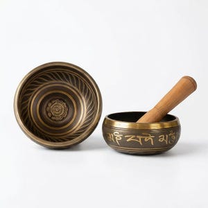 Può includere: Due ciotole tibetane color bronzo e un battente in legno. La ciotola più grande ha cerchi concentrici e un motivo floreale al centro. La ciotola più piccola ha testo inciso sul bordo. Il battente è marrone chiaro.