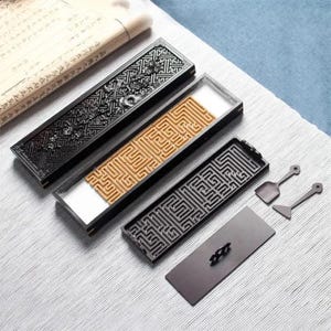Peut inclure: Ensemble de porte-encens et d'accessoires. Les porte-encens sont rectangulaires avec des sculptures détaillées, notamment un motif de labyrinthe et des motifs floraux. Les outils comprennent une petite pelle, un grattoir et un couvercle. Les articles sont noirs et marron.