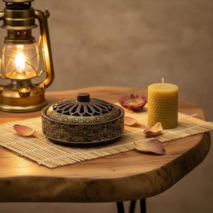 Peut inclure: Un brûleur d'encens décoratif avec un motif floral, une lanterne allumée et une bougie en nid d'abeille jaune sont posés sur une table en bois. Des pétales de fleurs séchées et un tapis en bambou complètent l'ambiance chaleureuse.