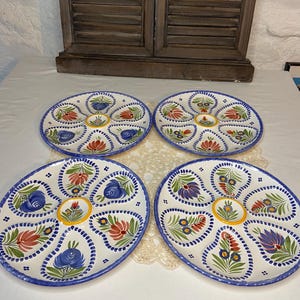 Könnte beinhalten: Vier ovale Austernplatten aus weißer Keramik mit blauem, rotem, gelbem und grünem Blumendesign. Jede Platte hat sechs Fächer und einen blauen Rand. Die Platten sind auf einer weißen Oberfläche angeordnet.