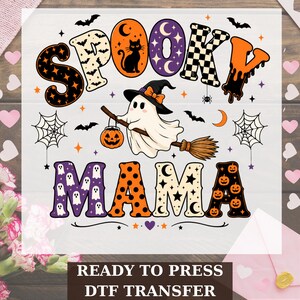May include: A graphic design featuring the text SPOOKY MAMA in bold, patterned letters. A white ghost wearing a witch hat flies on a broomstick, holding a jack-o'-lantern. The design includes bats, spiderwebs, stars, and moons in orange, purple, and black.