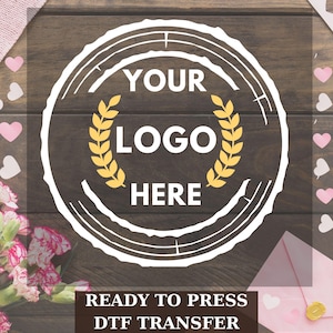 May include: A circular DTF transfer design featuring a white wood grain border, yellow laurel leaves, and the text YOUR LOGO HERE in white. Below the circle, the text READY TO PRESS DTF TRANSFER is displayed in white on a dark brown background.