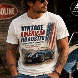 Op de afbeelding: Een wit t-shirt met korte mouwen en een grafische print met de tekst VINTAGE AMERICAN ROADSTER, CLASSIC PERFORMANCE, BUILT FOR THE DRIVE, een blauwe sportwagen met witte racestrepen en een verweerde Amerikaanse vlag op de achtergrond.