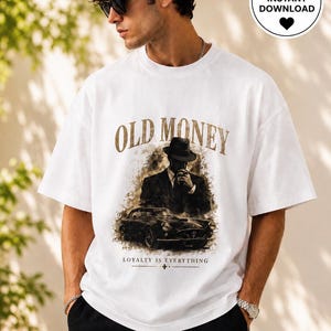 Könnte beinhalten: Weißes T-Shirt mit dem Schriftzug "OLD MONEY" in Gold. Das Shirt zeigt eine Grafik eines Mannes in Anzug und Hut mit einem Oldtimer. Der Text "LOYALTY IS EVERYTHING" steht darunter.