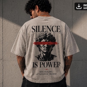 Può includere: Una t-shirt beige oversize con una grafica nera di una testa di statua classica sul retro. Una pennellata rossa orizzontale copre gli occhi. Il testo recita SILENCE IS POWER e MOVE IN SILENCE, LET SUCCESS BE THE NOISE in carattere nero.