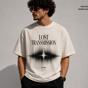 以下が含まれることがあります： 「LOST TRANSMISSION」の黒い文字と白黒の音波グラフィックがプリントされたクリーム色のTシャツ。「88.5 MHZ」の文字が下にあります。ゆったりとしたフィット感のTシャツです。