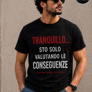 May include: A black short-sleeved t-shirt featuring the red and white text "TRANQUILLO... STO SOLO VALUTANDO LE CONSEGUENZE" printed on the chest, accompanied by a horizontal red line and three red dots positioned below the text.