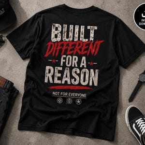 May include: A black short-sleeve t-shirt featuring the white and red distressed text BUILT DIFFERENT FOR A REASON, with the smaller text NOT FOR EVERYONE below it, accompanied by three circular icons containing a barbell, a target, and a star.
