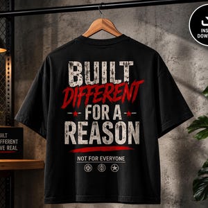 May include: A black t-shirt featuring the white distressed text BUILT DIFFERENT FOR A REASON with the word DIFFERENT in red. Below is the text NOT FOR EVERYONE and three small circular icons. The design is centered on the back of the garment.