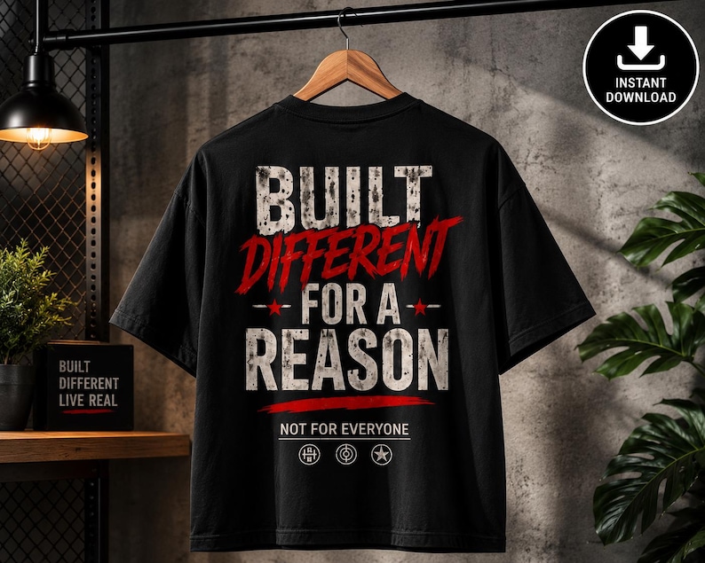 May include: A black t-shirt featuring the white distressed text BUILT DIFFERENT FOR A REASON with the word DIFFERENT in red. Below is the text NOT FOR EVERYONE and three small circular icons. The design is centered on the back of the garment.