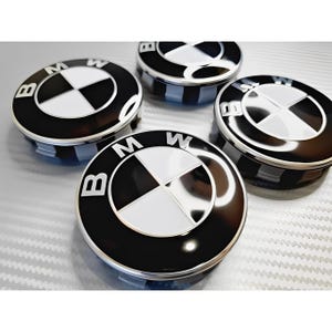 Könnte beinhalten: Vier schwarz-weiße BMW-Radnabenabdeckungen. Jede Kappe zeigt das BMW-Logo, ein kreisförmiges Emblem mit einem schwarzen Außenring, einer weißen Mitte und einem Vier-Quadranten-Design. Die Kappen sind auf einer reflektierenden Oberfläche angeordnet.