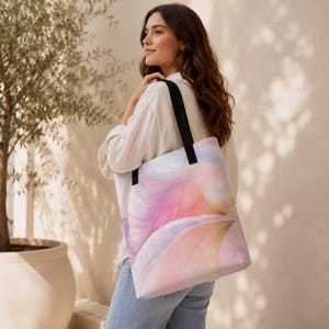 Può includere: Una borsa tote con un delicato design ad acquerello astratto nei toni del rosa pastello, lavanda e pesca. La borsa presenta due robuste tracolle in tessuto nero e una forma rettangolare, offrendo un interno spazioso per vari oggetti.