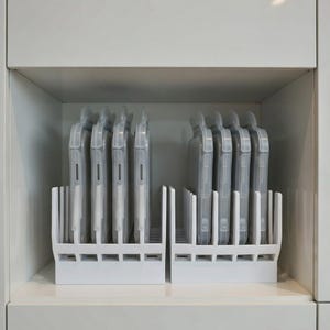Peut inclure: Deux organisateurs en plastique blanc, chacun contenant plusieurs coques de téléphone en plastique transparent. Les étuis sont dans des emballages individuels. Les organisateurs sont sur une étagère blanche à l'intérieur d'une armoire blanche.