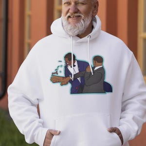 May include: White hoodie with a cartoon illustration of a man slapping another man. The illustration shows a man in a blue suit slapping another man in a grey suit. The slapped man is spitting. The hoodie has a front pocket.