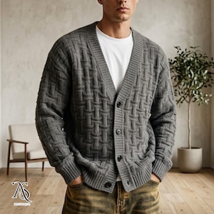 May include: A gray, button-down cardigan sweater with a woven pattern. The sweater has a V-neck and long sleeves. The model is wearing a white t-shirt underneath and jeans. The sweater has three black buttons.
