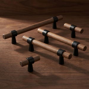 May include: A collection of five cabinet pulls and knobs featuring cylindrical brown wood bars accented with matte black metal mounting posts. The set includes one long pull, two medium pulls, and two small knobs arranged on a flat surface.