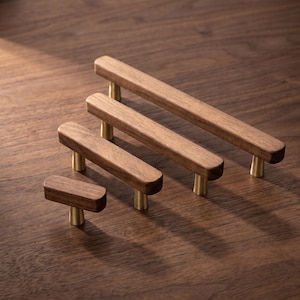 May include: Four cabinet pulls of varying lengths arranged in a row, each featuring a smooth, rectangular dark brown wooden handle supported by two small, conical brushed brass metal posts, except for the smallest pull which has one post.