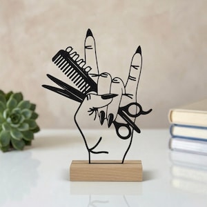 Peut inclure: Une sculpture en métal noir découpé représentant une main faisant un geste rock-and-roll, tenant un peigne et une paire de ciseaux. Le peigne est gravé avec le nom anna. La sculpture est montée sur une base rectangulaire en bois clair.