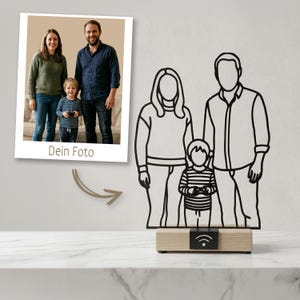 Puede incluir: Una escultura de alambre de metal negro que representa a una familia de tres personas, compuesta por dos adultos y un niño, montada sobre una base rectangular de madera clara. La base tiene una placa negra con un icono de Wi-Fi blanco.